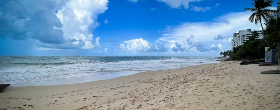 Condado Beach in San Juan, Puerto Rico — wide sandy shore with calm Atlantic waves, palm trees, and Condado skyline on a sunny day
